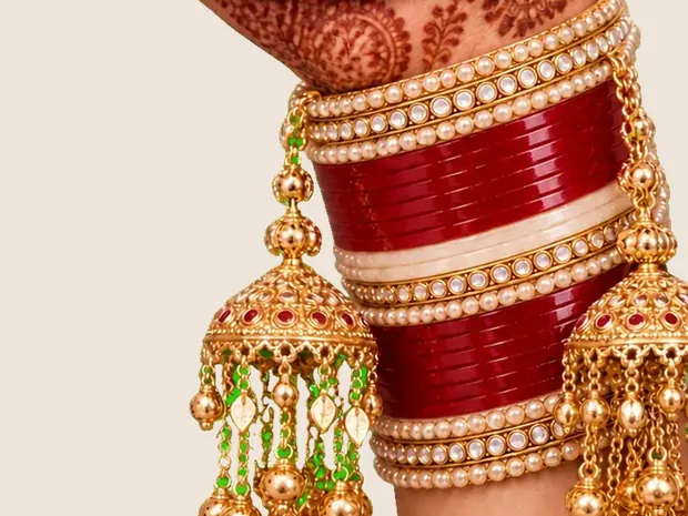 A bride's wrist with a red chooda and gold kaleere