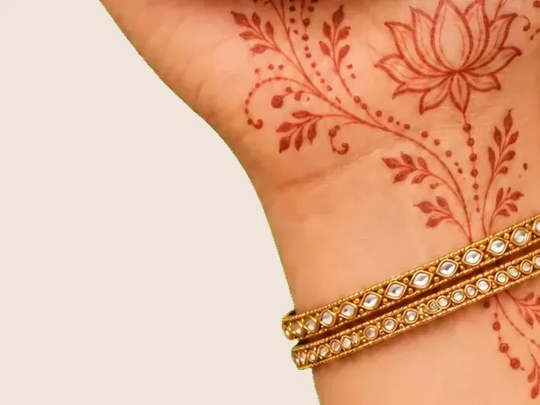 A bride's hand with a lotus mehendi design and gold bangles