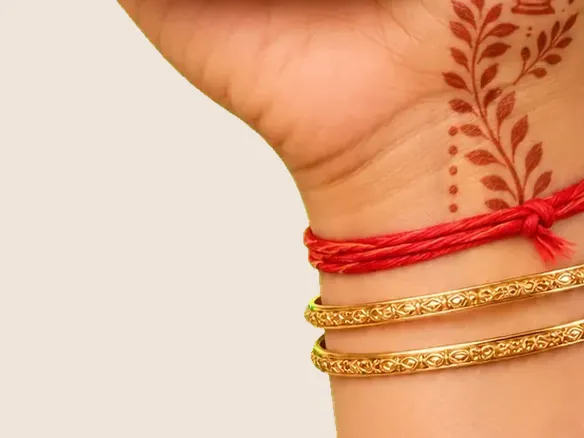 A wrist tied with a red kalava thread above gold bangles