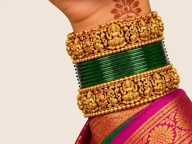 A wrist in gold temple bangles and green glass bangles over a pink silk saree